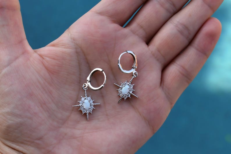 A hand holding a pair of silver earrings with star-shaped charms.