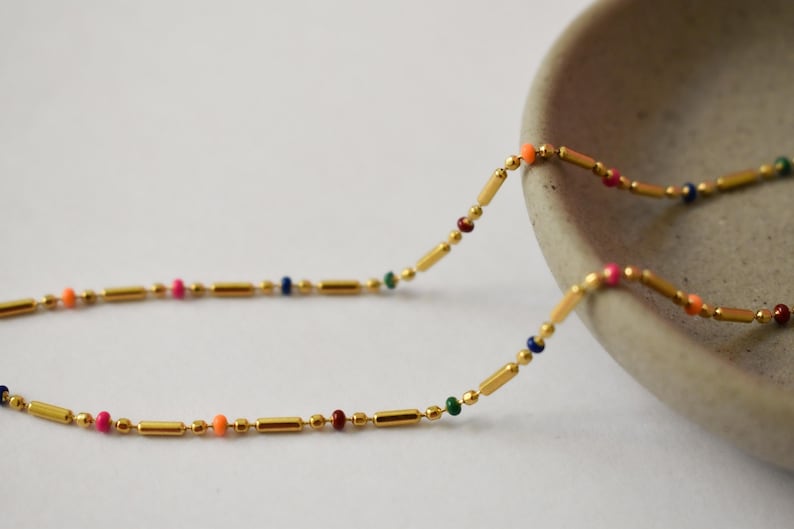 a long beaded necklace sitting next to a bowl