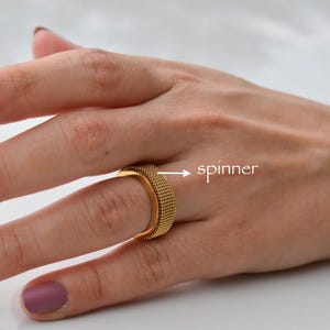 A close-up of a hand wearing a gold ring with a spinner design, and the word "spinner" is visible.
