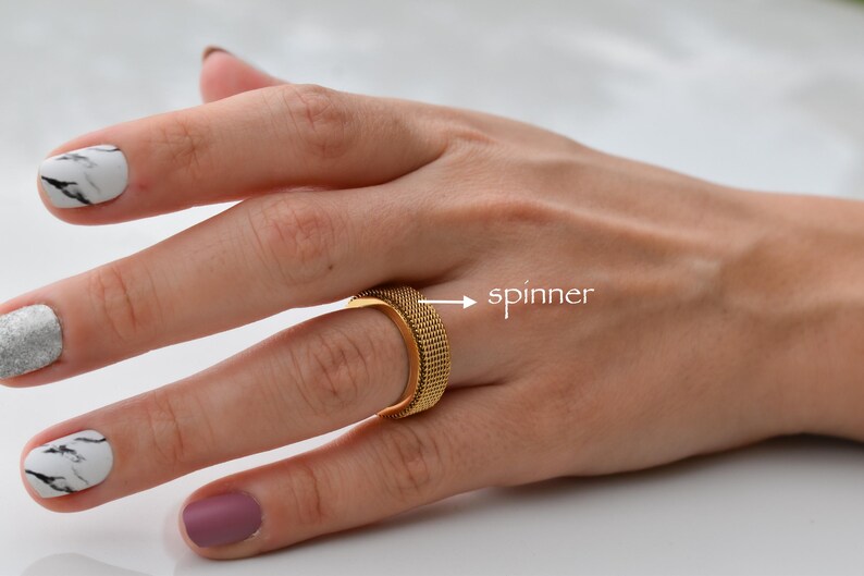 A close-up of a hand wearing a gold ring with a spinner design, and the word "spinner" is visible.