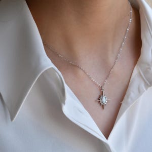 A close-up view of a person wearing a white collared shirt and a necklace with a pendant.