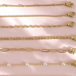 a collection of gold-colored necklaces and chains arranged on a pink background.