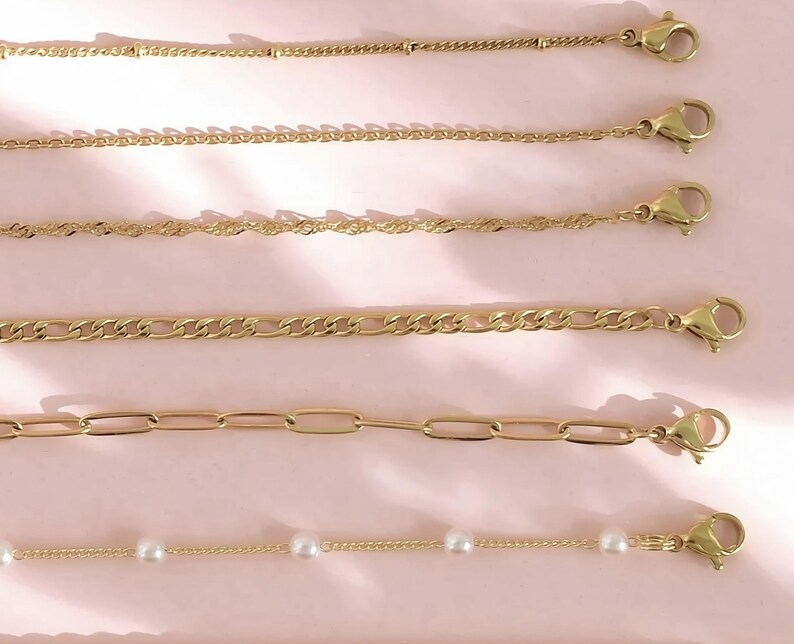 a collection of gold-colored necklaces and chains arranged on a pink background.