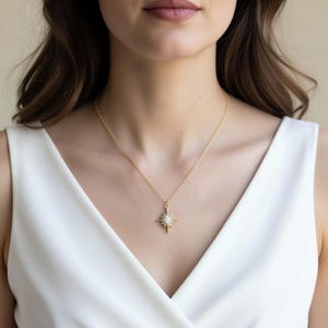A woman wearing a white sleeveless top and a gold necklace with a pendant.