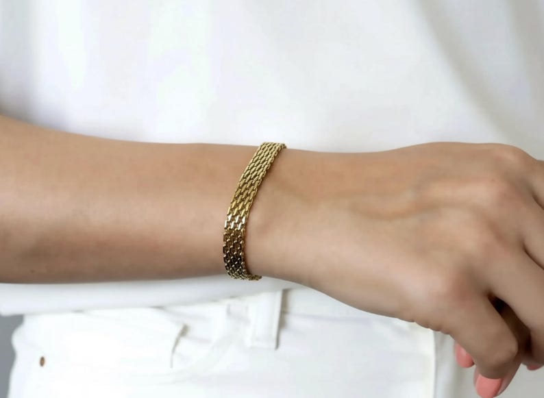 A gold bracelet is worn on a person's wrist.