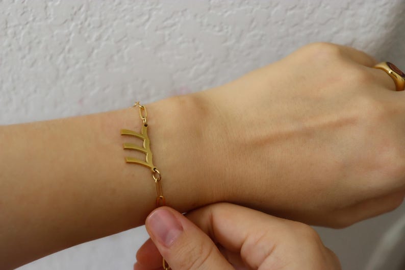 A person's wrist wearing two gold-colored bracelets with Chinese characters on them.