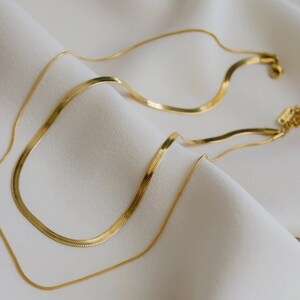 a pair of gold-colored necklaces with a shiny, metallic appearance, resting on a white fabric surface.