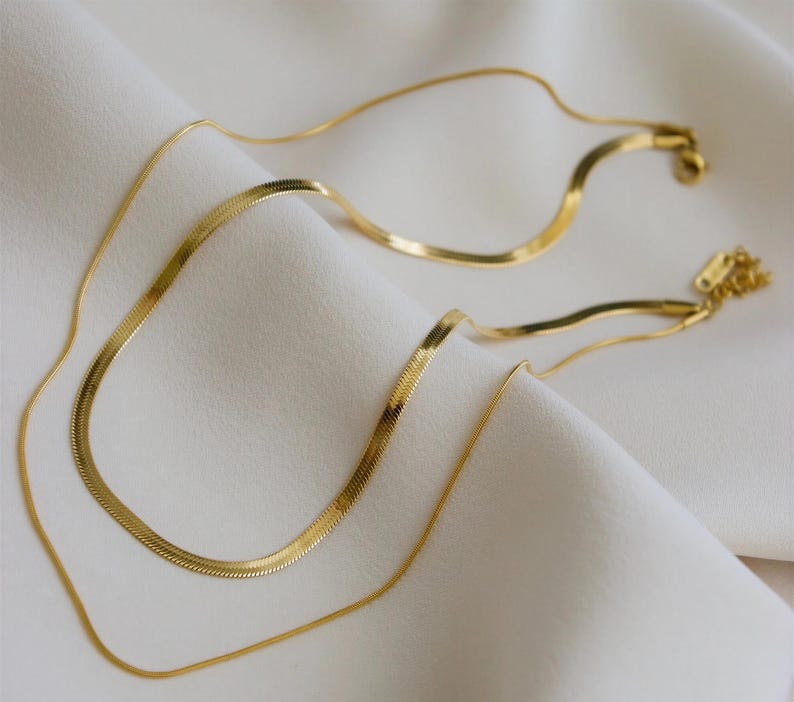 a pair of gold-colored necklaces with a shiny, metallic appearance, resting on a white fabric surface.