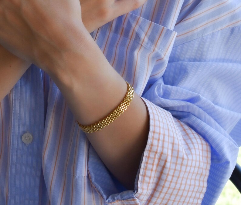 A close-up of a person's hands wearing multiple rings and bracelets, with their fingers crossed.