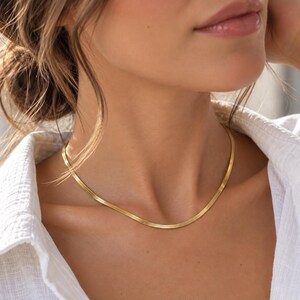 A close-up of a woman's neck and chest area wearing a gold necklace.