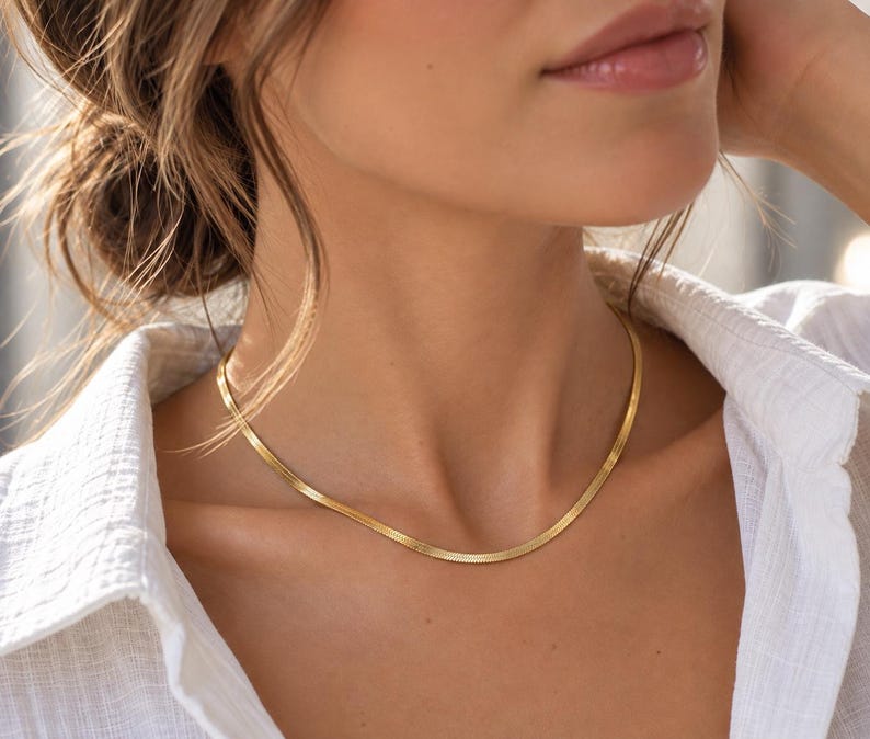A close-up of a woman's neck and chest area wearing a gold necklace.
