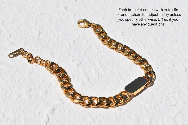 A gold-colored bracelet with a black rectangular charm is shown against a white background.