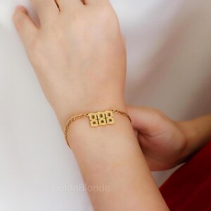 A close-up of a person's hand wearing a gold ring and bracelet, with a red dress visible in the background.