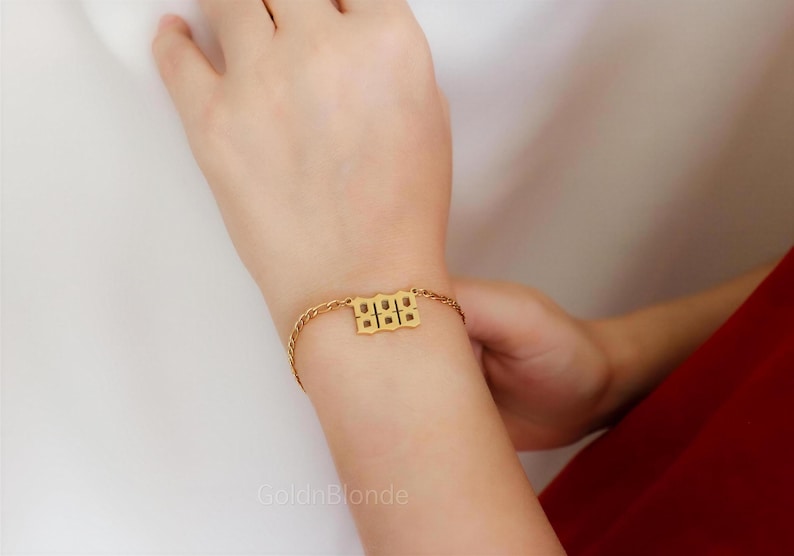 A close-up of a person's hand wearing a gold ring and bracelet, with a red dress visible in the background.