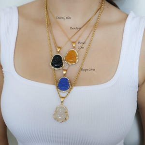 A woman wearing a white tank top with multiple necklaces around her neck.