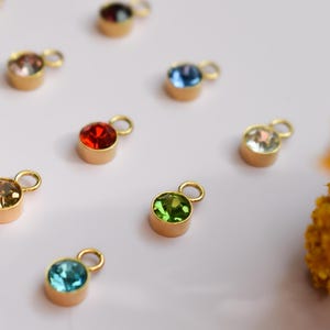 a collection of colorful gemstone charms or pendants, each with a unique shape and size, arranged on a white background.
