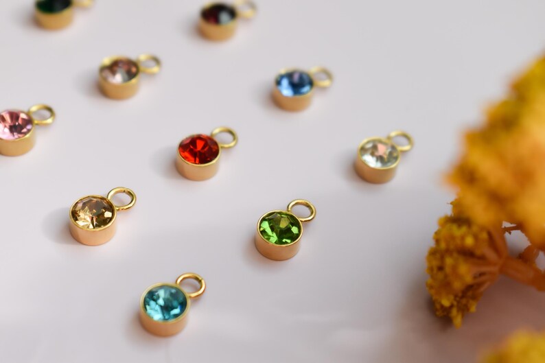 a collection of colorful gemstone charms or pendants, each with a unique shape and size, arranged on a white background.