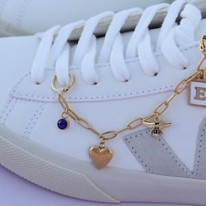 a pair of white sneakers with gold chains and charms