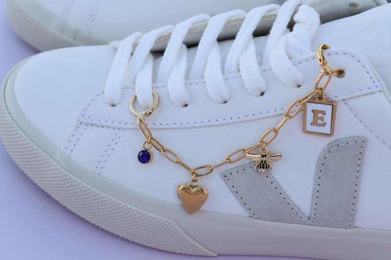 a pair of white sneakers with gold chains and charms