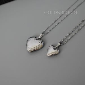 May include: Two silver-toned heart-shaped lockets on matching twisted chains. Each locket features an ornate, engraved border surrounding a smooth, polished centre. The text GOLDNBLONDE is visible in the upper right corner of the image.