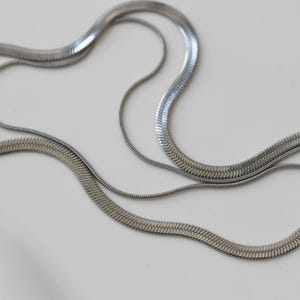 a close-up view of several silver-colored metal necklaces arranged on a white surface.