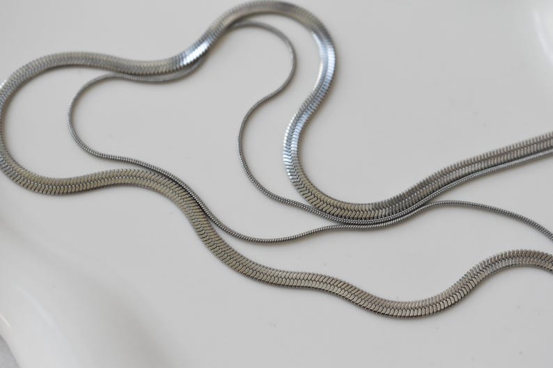 a close-up view of several silver-colored metal necklaces arranged on a white surface.