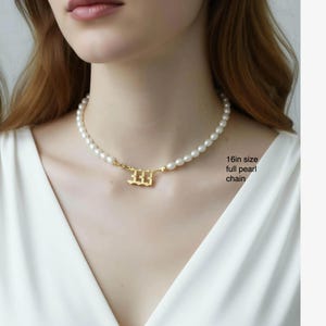A close-up of a woman wearing a pearl necklace with a gold-colored pendant.