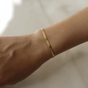 A gold bracelet is worn on a person's wrist.