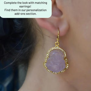 A close-up of a person's ear wearing a pair of gold earrings with a purple stone.