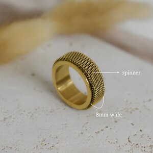 A close-up image of a gold ring with a textured surface, placed on a white surface with a blurred background.