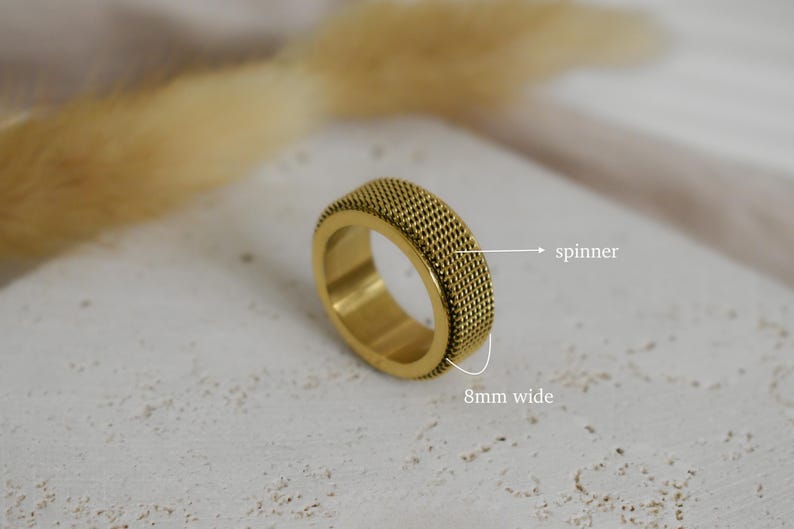 A close-up image of a gold ring with a textured surface, placed on a white surface with a blurred background.