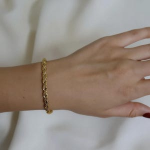 A gold bracelet is worn on a person's wrist.