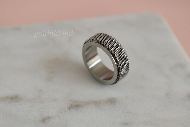 A silver ring with a textured surface sits on a white marble surface.