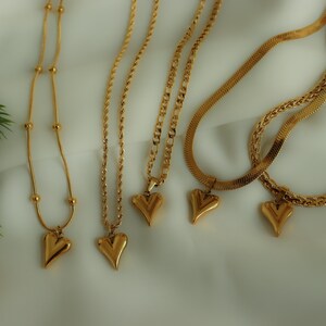 a collection of gold heart-shaped pendants and necklaces arranged on a white background.