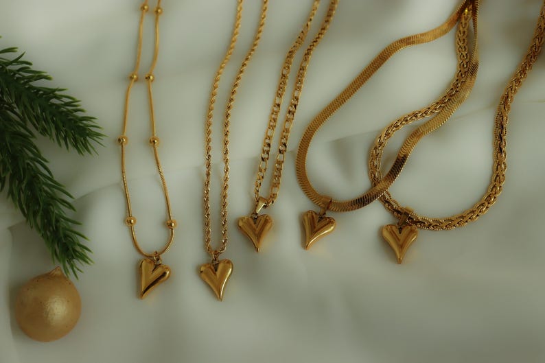 a collection of gold heart-shaped pendants and necklaces arranged on a white background.