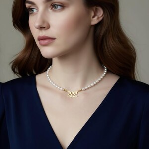 A woman wearing a navy blue blouse and a pearl necklace with a gold-colored pendant.
