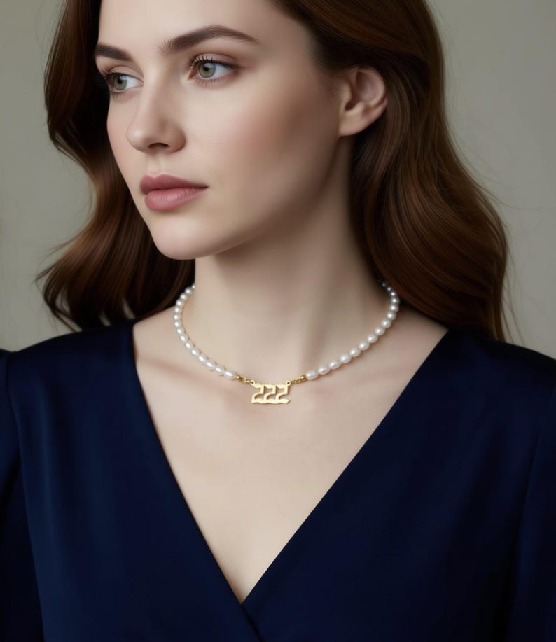 A woman wearing a navy blue blouse and a pearl necklace with a gold-colored pendant.