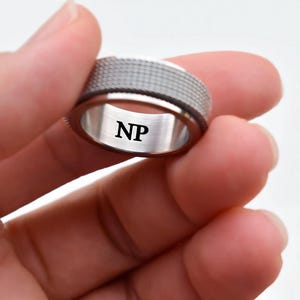 A close-up image of a person's hand holding a silver ring with the initials "NP" engraved on it.
