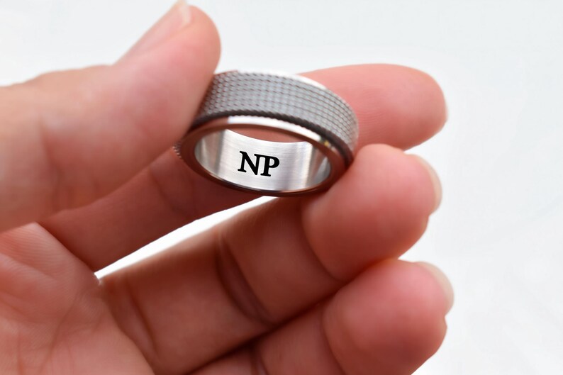 A close-up image of a person's hand holding a silver ring with the initials "NP" engraved on it.
