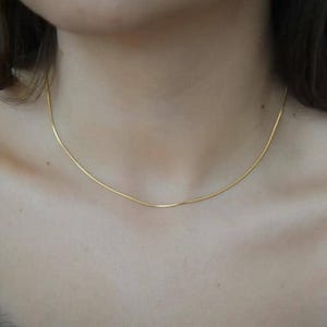 A close-up view of a woman's neck and chest area, showing a delicate gold necklace with a thin chain.
