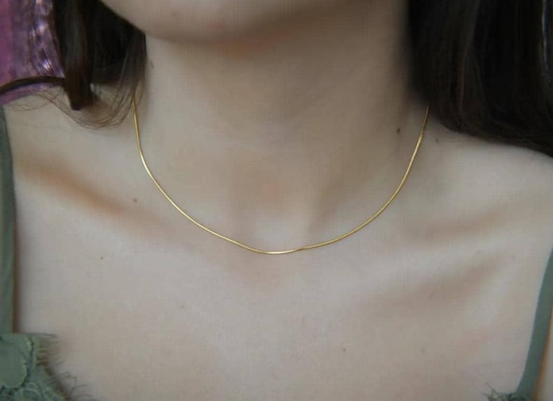 A close-up view of a woman's neck and chest area, showing a delicate gold necklace with a thin chain.