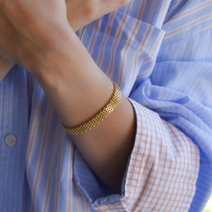 A close-up of a person's hands wearing multiple rings and bracelets, with their fingers crossed.