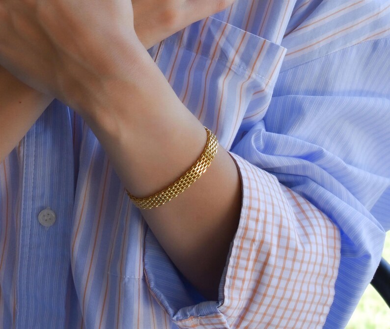 A close-up of a person's hands wearing multiple rings and bracelets, with their fingers crossed.