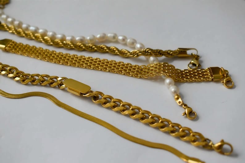 a collection of gold necklaces and bracelets arranged on a white background.