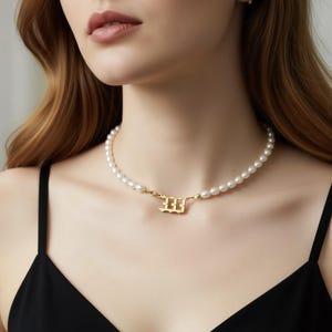 A close-up of a woman wearing a pearl necklace with a gold-colored pendant.