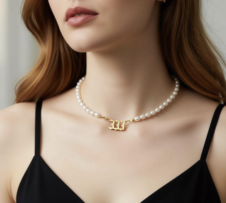 A close-up of a woman wearing a pearl necklace with a gold-colored pendant.