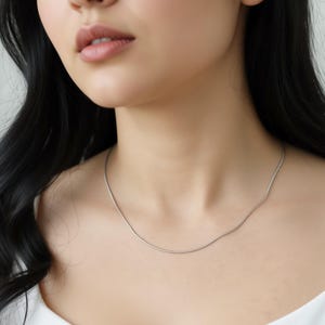 A close-up of a woman's neck and chest area, with a silver necklace visible.