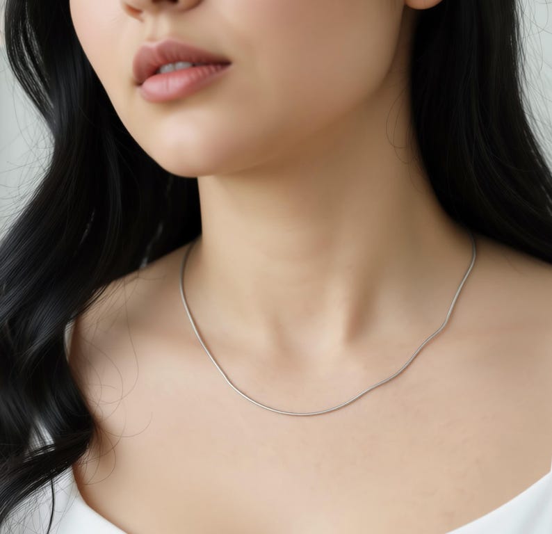 A close-up of a woman's neck and chest area, with a silver necklace visible.