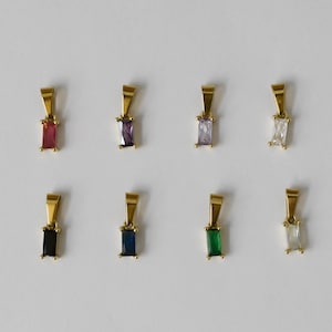 May include: Eight gold-colored pendant necklaces with rectangular gemstones in various colors: red, purple, light purple, white, black, blue, green, and clear. The pendants are displayed on a white background.