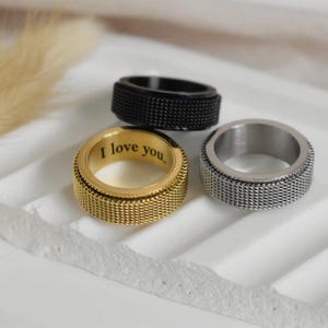 Three rings are displayed on a white surface, with one ring featuring a message engraved on it.